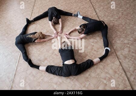 Horizontal high angle shot of unrecognizable dancers wearing black clothes doing stretching exercise on floor Stock Photo