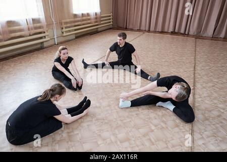 Horizontal high angle shot of four professional dancers starting workday with doing warming up exercise together Stock Photo