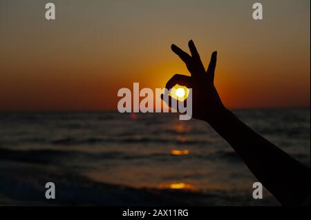 OK Sign with hands against the sunset, sunrise on the sea Stock Photo