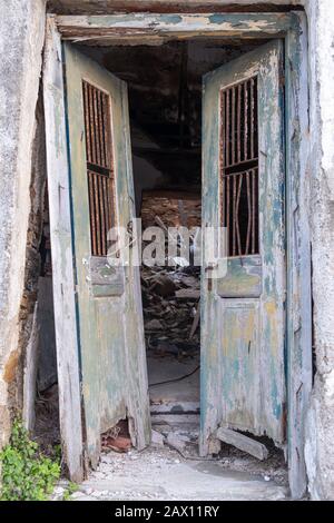 Old and destroyed double open door. Wooden, peeled, unlocked doorway in an abandoned and ruined house. Danger of collapse, vertical view. Stock Photo
