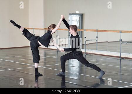 Young man and woman in black rehearsing contemporary partner dance in studio, horizontal shot Stock Photo