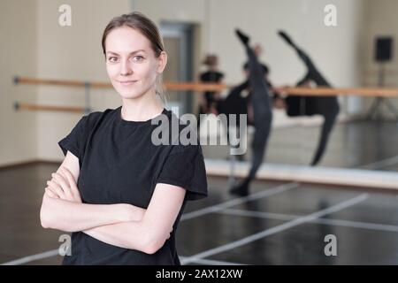 Horizontal medium portrait of young woman wearing black T-shirt standing with arms crossed in rehearsal studio looking at camera Stock Photo