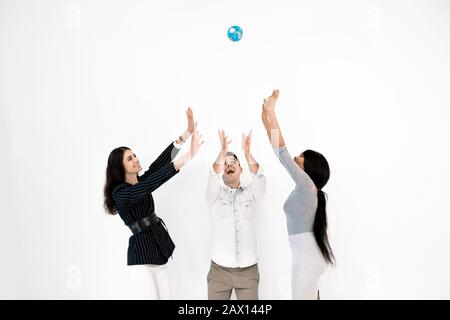 Group of three multiethnical international happy people throwing up little globe earth and looking up while it is levitating in the air. Education, tr Stock Photo