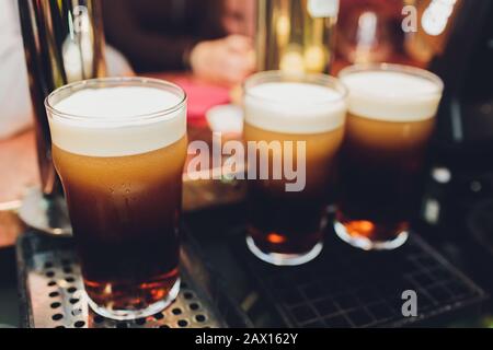 Close up of a male bartender dispensing draught beer in a pub holding a large glass tankard under a spigot attachment on a stainless steel Stock Photo