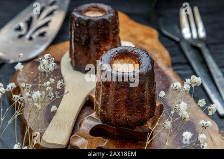 Cannelés (Canelés) de Bordeaux Recipe is a small pastry with rum and vanilla on a wooden plate. Traditional French sweet dessert. tasty snacks. Obliqu Stock Photo