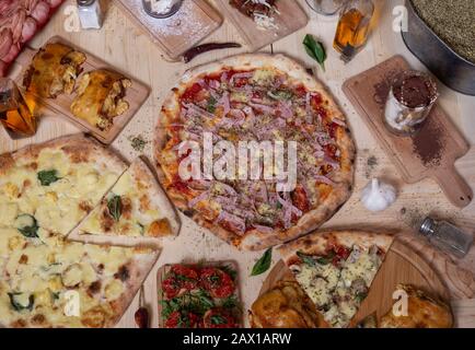 Aerial view of delicious varieties of freshly prepared Neapolitan Mediterranean pizzas and tapas on wooden table. Stock Photo