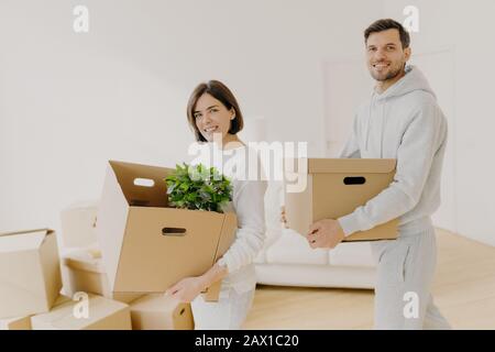 Buying real estate and mortgage loan concept. Glad woman and man carry cardboard boxes move into new home, busy with unpacking. Family property owners Stock Photo