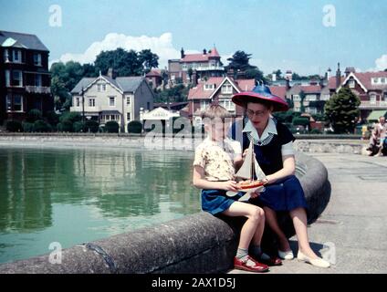 Five year old boy with his mother looking at a Star pond yacht sitting on the edge of a seaside boating pool in the summer wearing red sandals Stock Photo