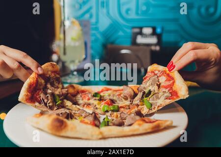 Close up female hand holding, taking slice, piece of pizza from box, friends sitting together in cafe, spending free time, eating Italian fast food, e Stock Photo
