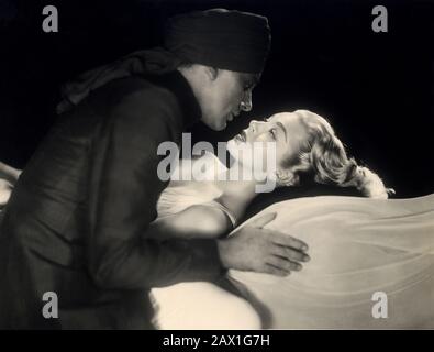 1955 , USA : The movie actor RICHARD BURTON with LANA TURNER in The Rains of Ranchipur  ( Le piogge di Ranchipur )  by Jean Negulesco , from a novel by Louis Bromfield - MOVIE - CINEMA - FILM - lovers - innamorati - amanti - profilo - profile - kiss - bacio - bionda - blond hair - blondie - capelli biondi - turban - turbante - embrace - abbraccio ---- Archivio GBB Stock Photo