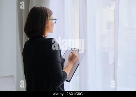 Mature woman couch taking notes standing near window in office Stock Photo