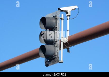 Black traffic light signal and traffic camera on overhead metal pole against blue sky Stock Photo