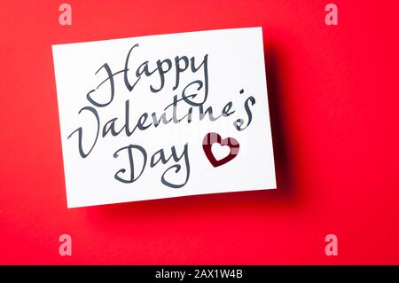 Handwritten Happy Valentine's Day message in informal calligraphic script on white card sitting on red background Stock Photo