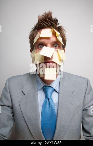 Exhausted office worker looking at the camera with yellow sticky notes all over his face Stock Photo