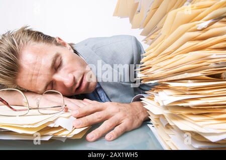 Tired office worker sleeping next an overwhelming stack of paperwork on his desk Stock Photo