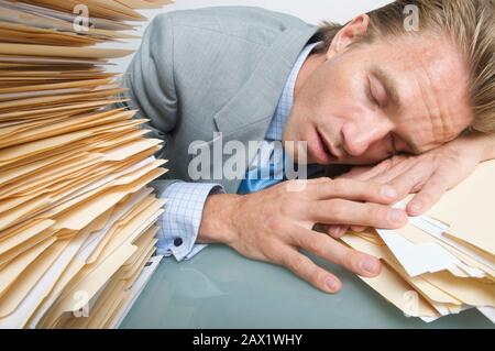 Tired businessman sleeping next an overwhelming stack of paperwork on his desk Stock Photo