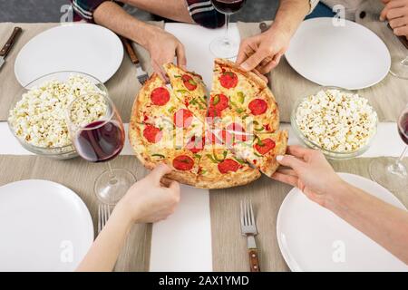 Horizontal high angle view shot of hands of unrecognizable people taking tasty pizza slices Stock Photo