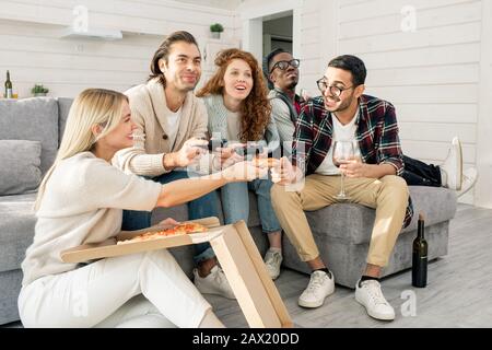 Horizontal shot of five friends having fun eating pizza and playing video games in modern apartment Stock Photo