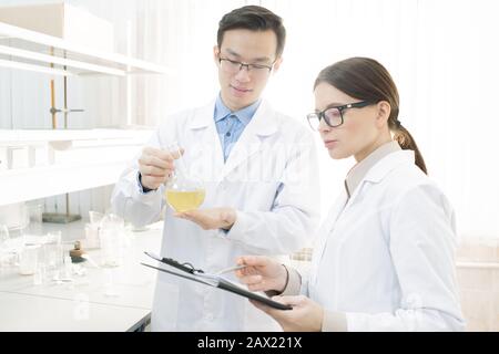 Two young medical scientists in white coats conducting research in modern laboratory, horizontal shot Stock Photo