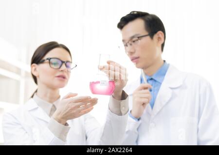 Horizontal low angle portrait of young Asian man and Caucasian woman wearing white coats analyzing chemical reaction Stock Photo