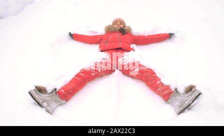 woman in a red suit on the snow in a winter park makes the figure of a snow angel in the park. Copy space text Stock Photo