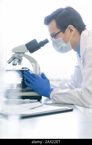 Vertical side view portrait of young male pharmacologist examining specimen chemical reaction using microscope in modern laboratory Stock Photo