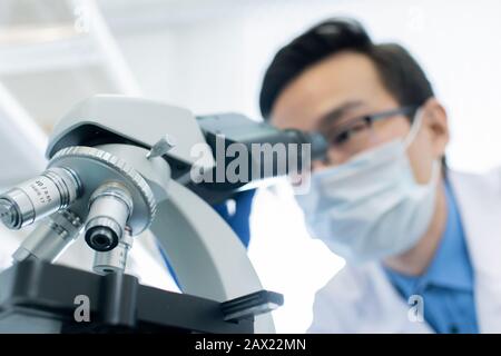 Unrecognizable male pharmacologist examining specimen using microscope in modern laboratory, horizontal shot Stock Photo