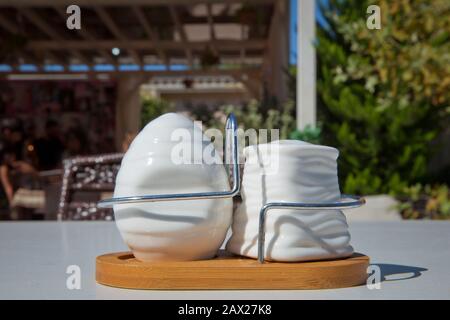 Ceramic pepper pot, salt shaker .Green blurred background in restaurant. white spicery set on white tablecloth . Ceramic salt and pepper shaker on Stock Photo