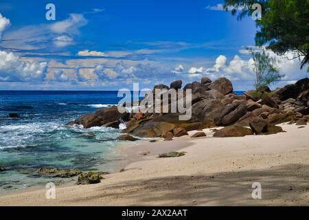 Ocean waves and granite rocks Takamaka beach, Mahe Island, Seychelles. Palmtrees, sand, crashing waves, beautiful shore, blue sky and turquoise water Stock Photo