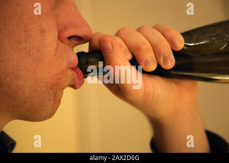 A white caucasian man drinking wine from a bottle home alone. Sad way to spend time, common for lonely, depressed and alcoholic people. Stock Photo