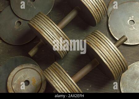 Vintage Rusty Dumbbells and Additional Plates on Scratched Rubber Floor Stock Photo