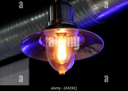 Luminous lamp in modern industrial loft style on dark background, artificial electric lighting. Stock close up photo for web, print, backgrouns and wallpaper. Stock Photo