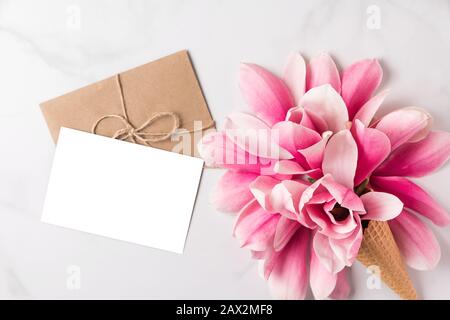 Blank white greeting card with spring pink magnolia flowers in waffle cone on white background. mock up. flat lay. top view. holiday festive backgroun Stock Photo