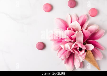 Spring pink magnolia flowers in waffle cone with macaroons on white background. spring concept. flat lay. top view. holiday festive background Stock Photo