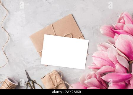 Creative layout made with pink magnolia flowers, greeting card, gift box and rope on gray background. Flat lay. Mock up. Wedding invitation. Spring ho Stock Photo