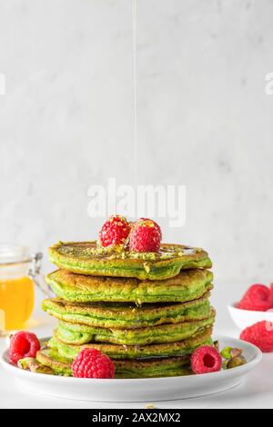 Green pancakes with matcha tea, raspberries, pistachios and honey. healthy breakfast. vertical orientation. close up