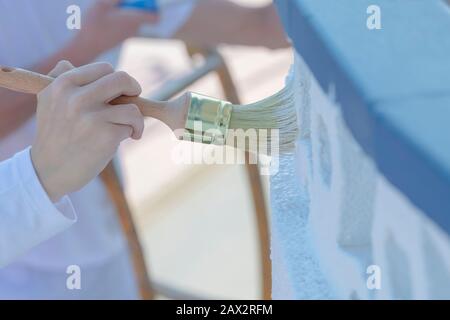 Close-up of a woman using a brush to paint a balcony outer wall with white paint on an out of focus background. Work concept. Stock Photo