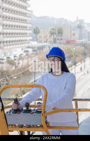 Close-up of a focused beautiful woman operating the control panel of a telescopic boom lift on an out of focus background. Work concept. Stock Photo