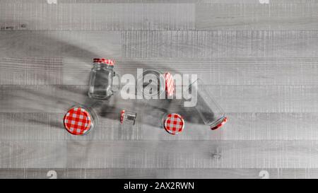 Top view of a collection of jars of assorted sizes with checkered lids on a wooden table. Rustic and artistic concept. Stock Photo