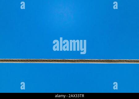 A power line connected to two transmission towers is taut, and viewed from below against a solid blue sky. Stock Photo