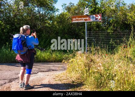 Woman hiker pilgrim photographing the ancient pilgrim’s way Via Francigena direction sign, Lazio, Italy Stock Photo