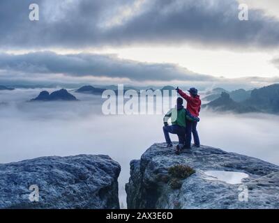 Lovely heterosexual Couple looking at far sunrise in heavy clouds. The dark night in foggy mountains ends. Stock Photo