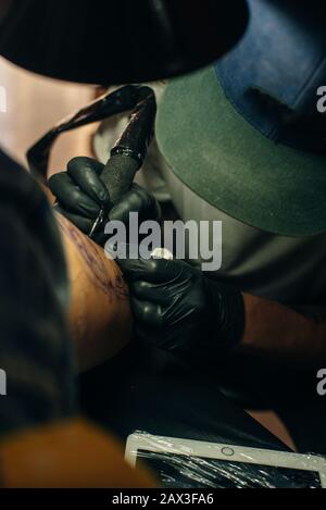 Close up of professional tattooer artist doing picture on hand of man by machine black ink from a jar.  Stock Photo
