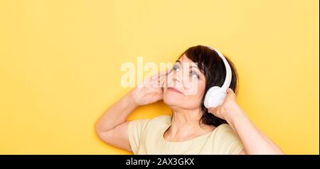 Beautiful Senior woman dancing and relaxing in the wireless headphones over yellow background Stock Photo