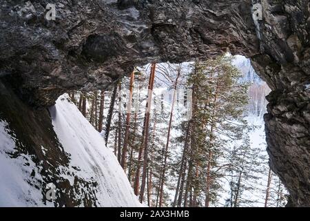 view of the snowy wooded river valley through a huge natural arch in the rock Stock Photo
