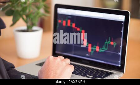 Man working on a laptop, with financial charts displayed. Businesss man at a computer, indoors shot. Stock Photo