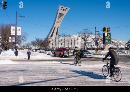 Montreal, CA - 8 February 2020: Two people riding bikes in winter, in front of Montreal Olympic Stadium Stock Photo