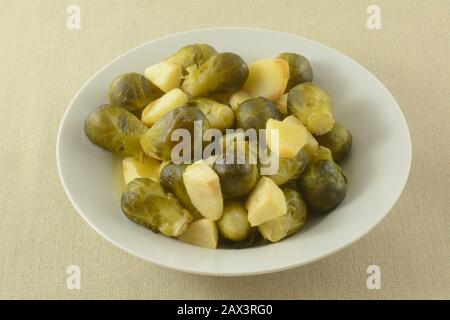 Side dish of cooked brussel sprouts and chopped apple in white bowl Stock Photo