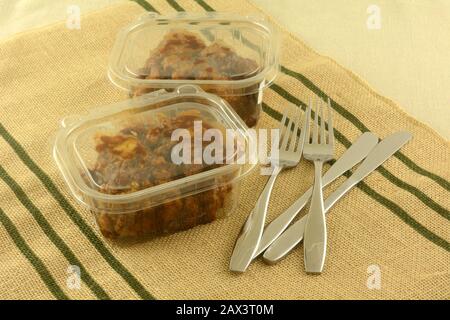 Two take out deli boneless chicken lunches in plastic containers with knives and forks on place mat Stock Photo