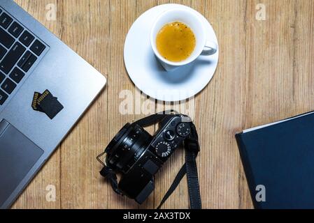Wooden desk table with camera, laptop, memory cards, espresso cup and clipboard. View from top. Stock Photo